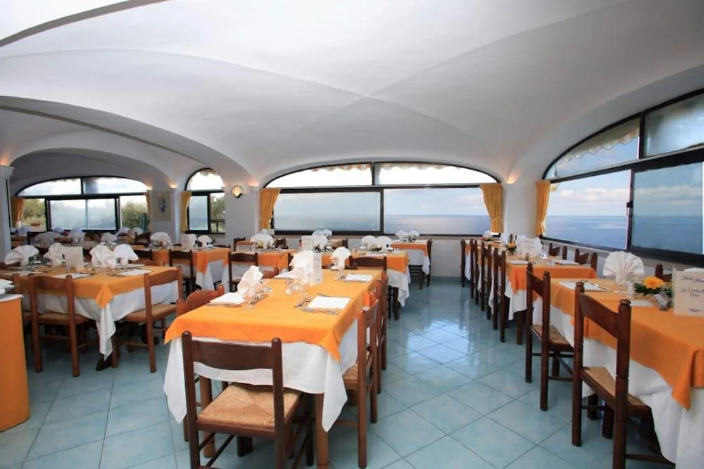 Sala ristorante con tavoli apparecchiati, tovaglie arancioni e grandi finestre con vista sul mare